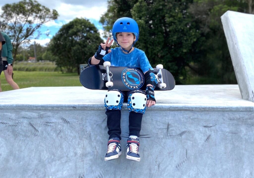 Skate Now skateboarder giving peace sign while wearing high-quality protective gear.