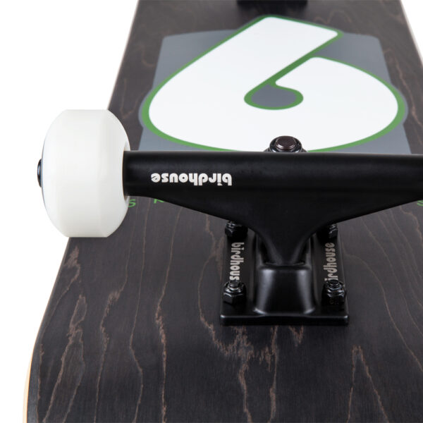 Close-up of black Birdhouse trucks and white wheels with Birdhouse branding in white on a black wood grain skateboard deck.