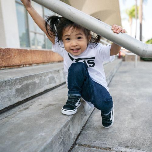 A young child wearing Vans skate shoes while playing on stairs and holding onto a handrail