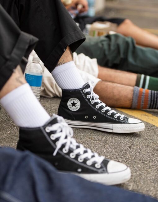 A pair of classic black and white Converse Chuck Taylor sneakers worn by a skateboarder.