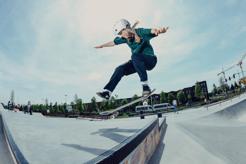 Teen skater in helmet and skate attire mid-kickflip up Euro gap