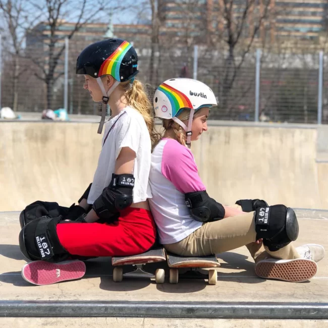 Two young skaters in skatepark, wearing Triple 8 certified sweatsavers and 187 pads, sitting on their boards back to back