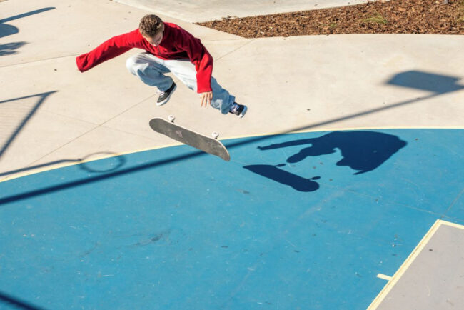 Skater performing a kickflip on a blue basketball court surrounded by new concrete